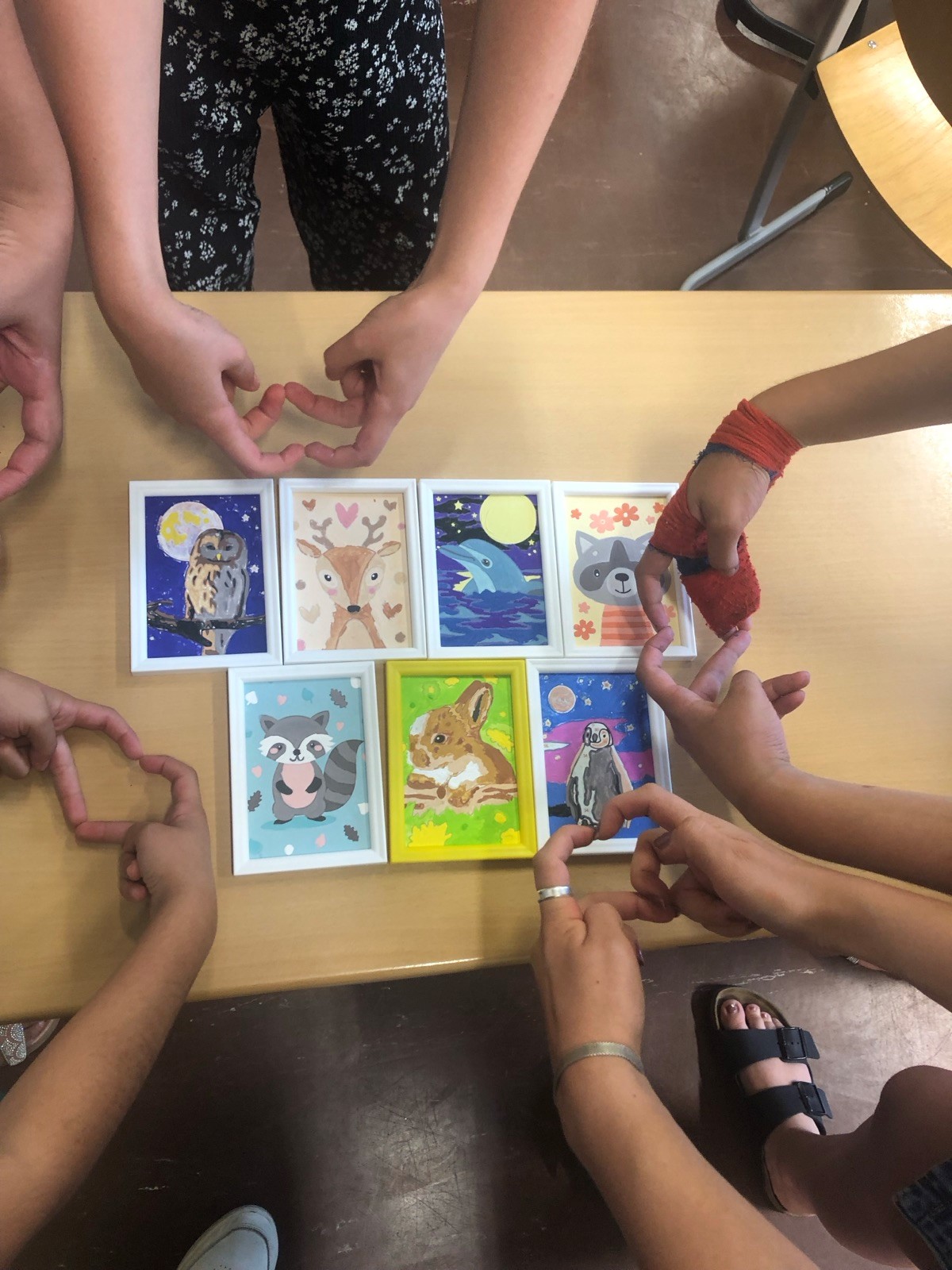 Es sind sieben bemalte malen-Nach-Zahlen Bilder mit Tiermotiven abgebildet. Es sind im kreis drei Paare von Händen, die eine Herzform mit ihren Fingern formen zu sehen.